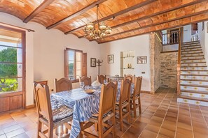 Un coin repas avec une table dressée pour six personnes, des chaises en bois, un lustre et une vue sur l’extérieur.