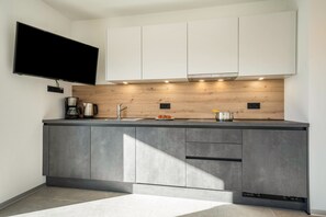 A modern kitchen with a flat-screen TV, wooden backsplash, and grey cabinetry.