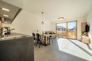 A modern kitchen with a dining area, large windows, and a view of the outside.