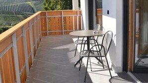 A balcony with a table and chairs, a view of a vineyard, and a modern building with large windows. - Apartment "Sunnig - Sonennschein" with Mountain View, Balcony & Wi-Fi (Völlan)