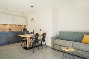 A modern kitchen with a dining area, a grey sofa, and a small round table with a plant.
