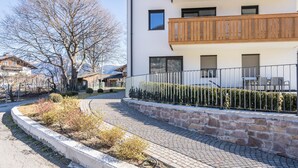Moderni rakennus, jossa on kivipäällysteinen kävelytie, puiset parvekkeet ja aidattu puutarha-alue.