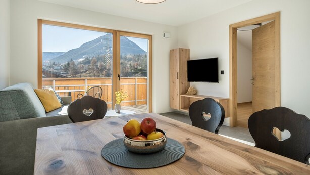 Een moderne woonkamer met een houten eettafel, een schaal fruit en een televisie aan de muur.