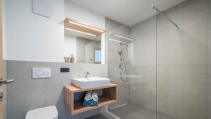 Een moderne badkamer met toilet, wastafel, spiegel en douche.