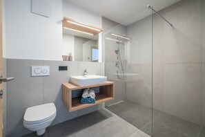 A modern bathroom with a toilet, sink, mirror, and shower.