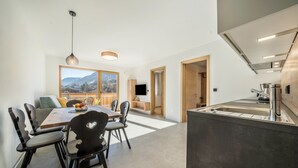 Een moderne keuken met een inbouw-kookeiland, een eethoek met een houten tafel en stoelen, en een groot raam met uitzicht op de bergen.