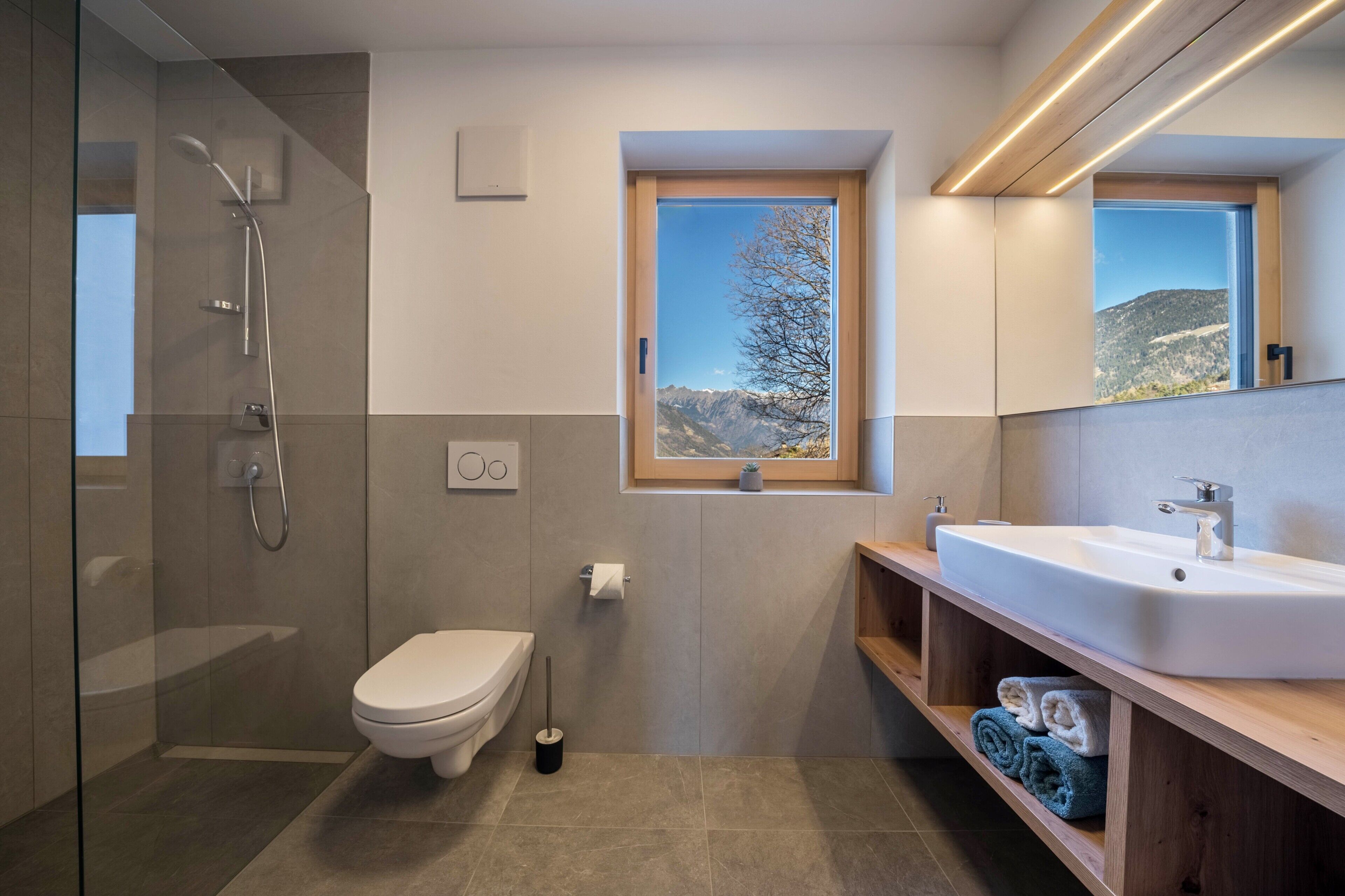 A modern bathroom with a shower, toilet, sink, and a window with a mountain view.