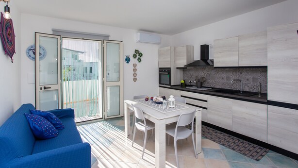 Un espace de vie compact comprenant un coin repas, une kitchenette et une porte-fenêtre coulissante donnant sur un espace extérieur.