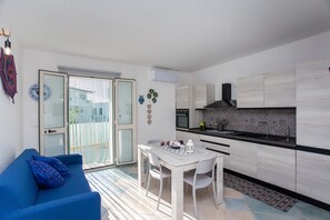 Ett kompakt bostadsutrymme med en matplats, ett litet kök och en skjutdörr i glas som leder ut till ett utomhusområde.