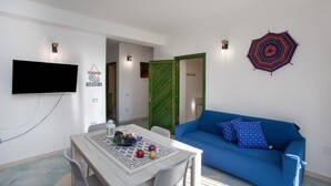 Une pièce avec une télévision, une table garnie de fruits, un canapé bleu et un élément décoratif mural.