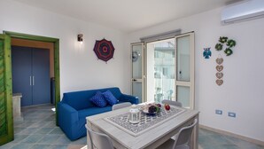 Une pièce avec un canapé bleu, une table à manger avec des chaises, un élément décoratif mural et une porte donnant sur une autre pièce.