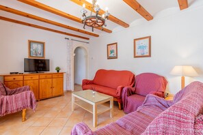 A living room with a sofa, armchair, TV, wooden cabinet, and a chandelier. - Villa 'Merced Planta Baja' with Mountain View, Private Pool and Wi-Fi (Calpe)