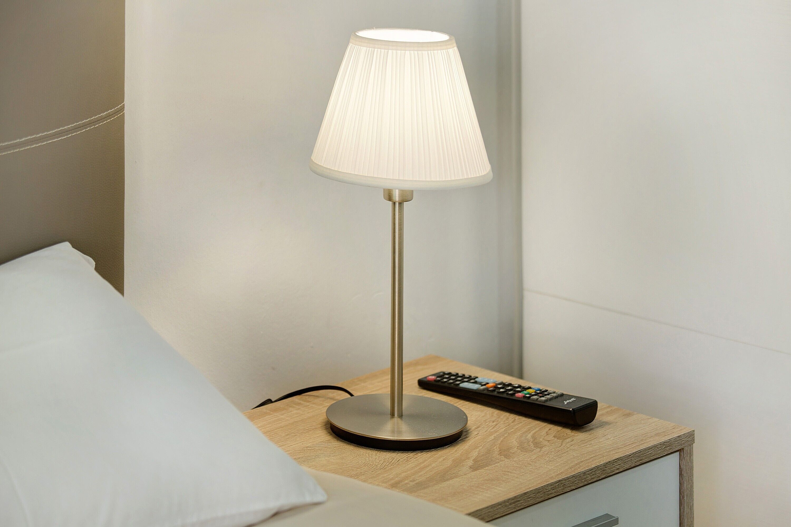 A bedside table with a lamp, a remote control, and a drawer.