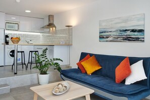 Une cuisine moderne équipée d’un four à micro-ondes, d’un évier et de tabourets, un canapé bleu avec des coussins et un tableau accroché au mur.