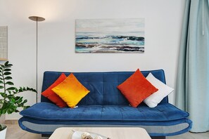 Un canapé bleu agrémenté de coussins colorés, un tableau représentant un paysage marin et une plante en pot.