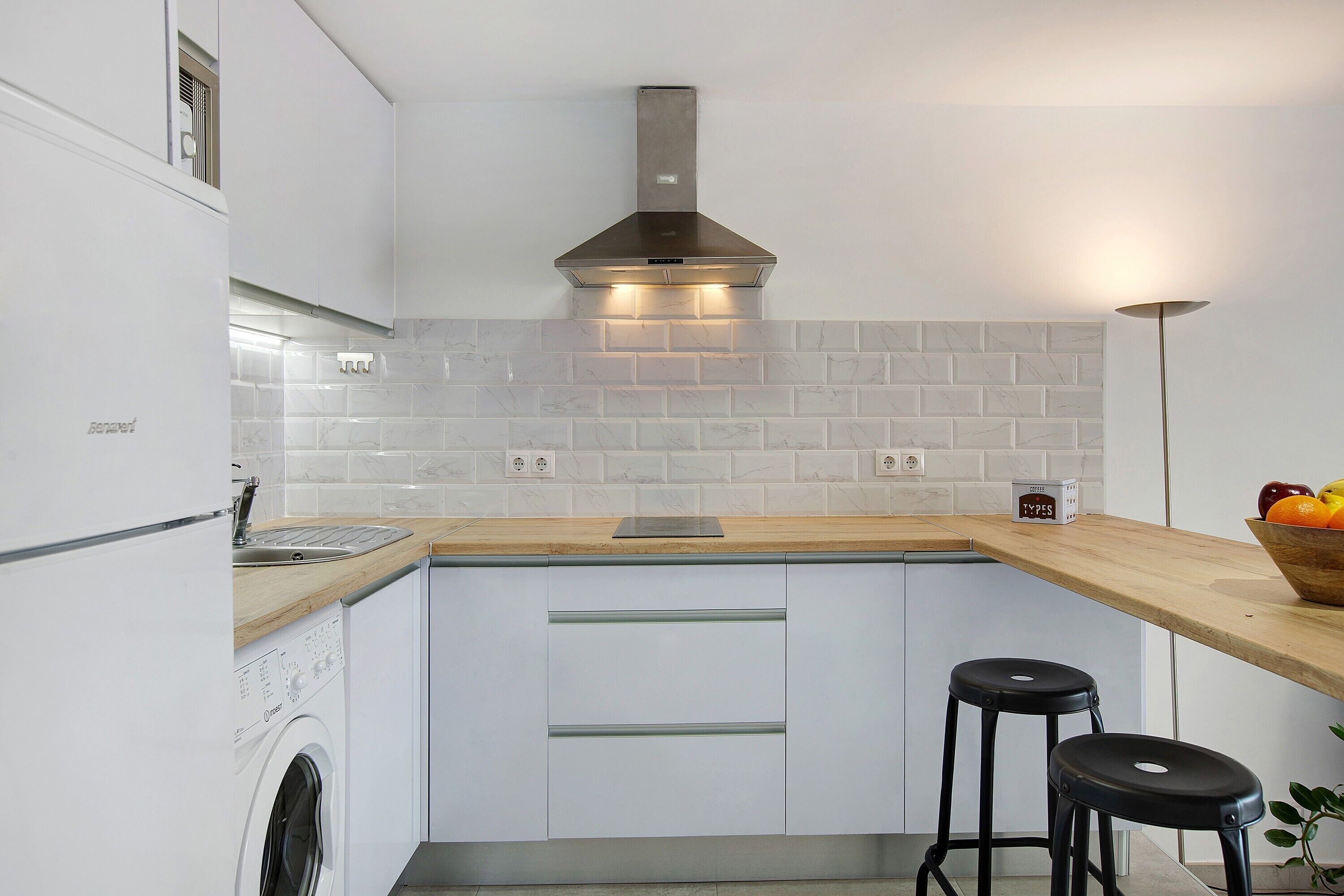 Una cocina moderna con lavadora integrada, campana de acero inoxidable y encimera de madera.