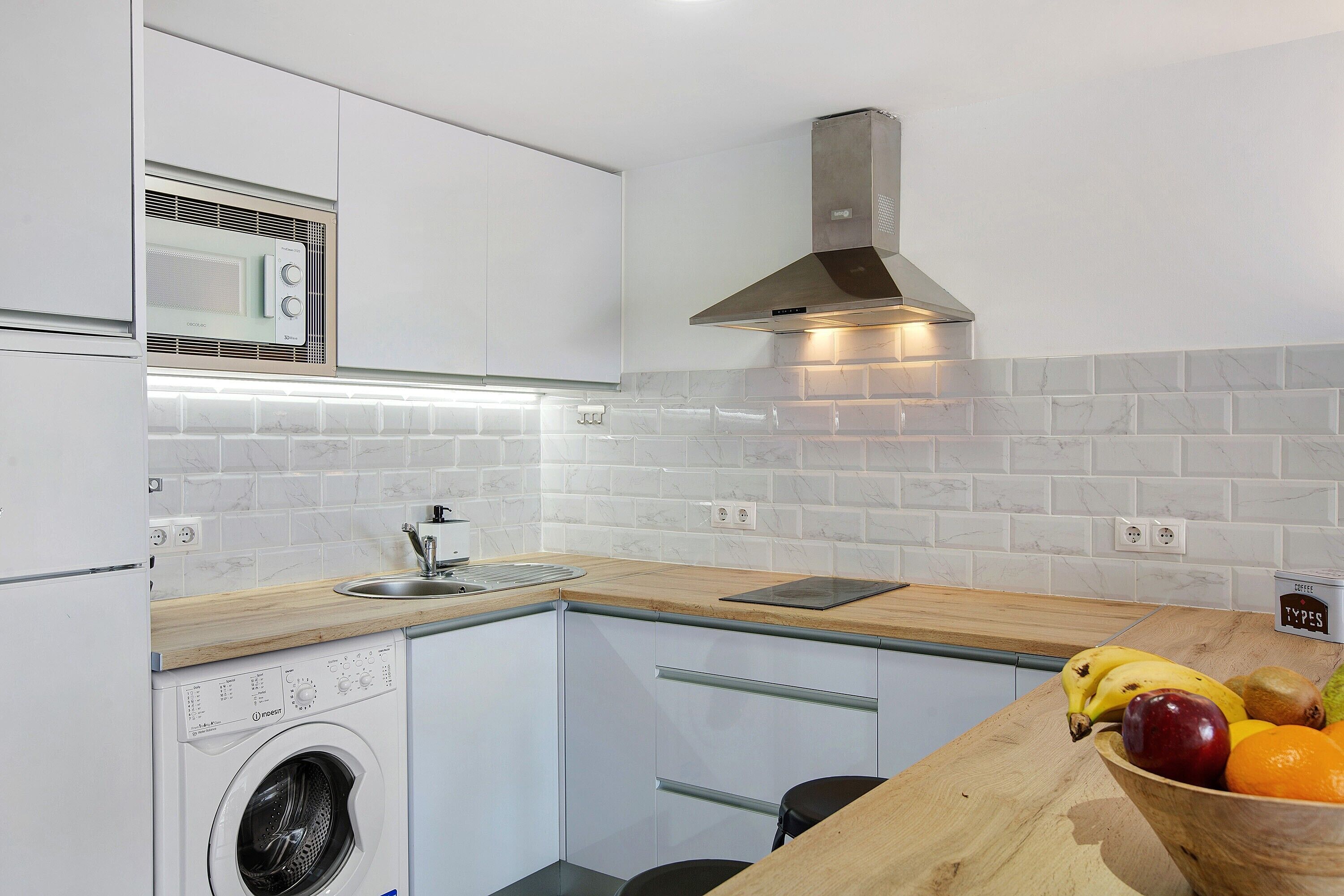 Una cocina compacta con lavadora integrada, microondas, campana extractora de acero inoxidable y encimera de madera.