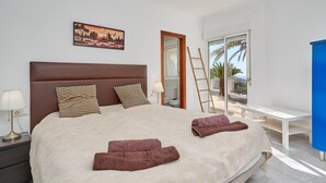 Un dormitorio con una cama grande, una mesita de noche, una lámpara, un cuadro, una ventana con vistas y un armario azul.