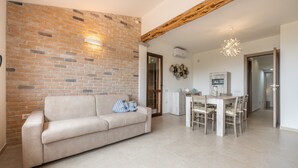 Un salon avec un mur en briques, un canapé, une table à manger avec des chaises et une poutre en bois au plafond.
