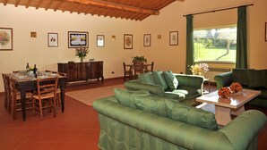 A dining area with a wooden table and chairs, a green sofa, and a window with curtains. - Villa in Lazio with Pool and Vineyards (Magliano Sabina)