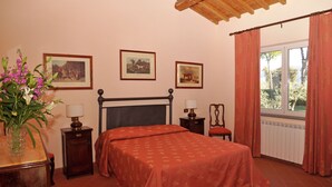 A bedroom with a bed, bedside tables, a lamp, a chair, and a window with curtains. - Villa in Lazio with Pool and Vineyards (Magliano Sabina)