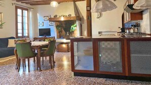 A cozy living room with a wooden ceiling, a dining area with a table and chairs, and a kitchen with a stove and cabinets. - Ca' Nadia Apartment  (Venice)
