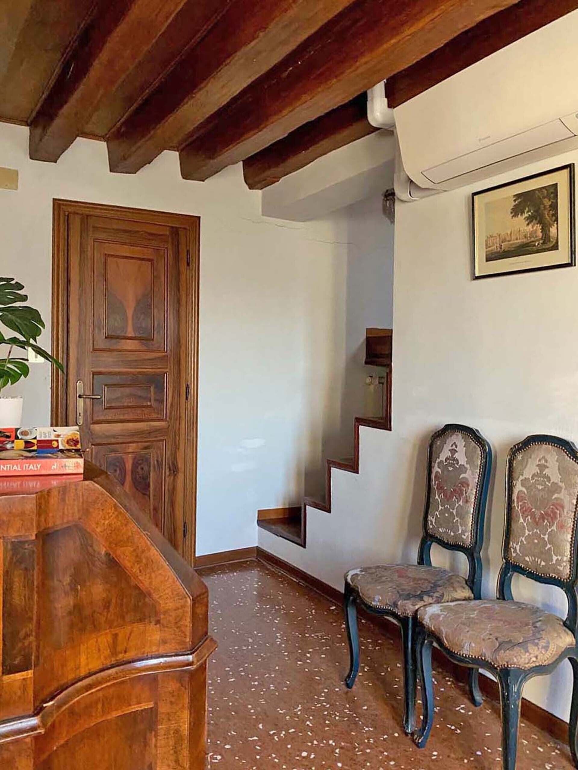 Una puerta de madera, una escalera y dos sillones tapizados en una habitación con paredes blancas y suelo de baldosas.