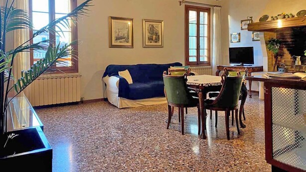 A cozy living room with a blue sofa, wooden ceiling beams, a dining table with chairs, and a television. - Ca' Nadia Apartment  (Venice)