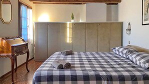 A bedroom with a checkered bedspread, a wooden headboard, a desk with a lamp, and a mirror. - Ca' Nadia Apartment  (Venice)