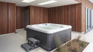 Un espace moderne aménagé à l’extérieur avec un bain à remous, une terrasse en bois, un petit banc en bois et un marchepied menant au bain.