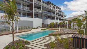 Un immeuble moderne à plusieurs étages, doté de balcons, d’une piscine et d’espaces verts aménagés.