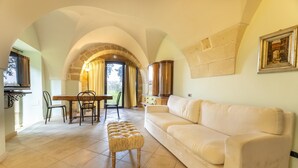 Amplia sala de estar con un sofá color beige, una mesa de comedor de madera con sillas y un arco de piedra que conduce a un balcón.