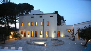 Une cour avec une piscine, des espaces de détente en plein air et un bâtiment dont les fenêtres sont illuminées.