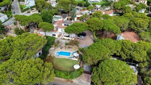 Vista aérea de un barrio residencial con piscina, rodeado de exuberante vegetación y casas con tejados rojos.