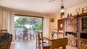 Un comedor con mesa y sillas de madera, vistas a través de ventanas amplias, y un mueble tradicional con objetos decorativos.