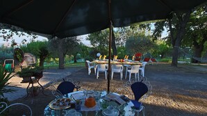 Un espace de restauration en plein air avec une table ronde en verre, des chaises blanches et un grand parasol.