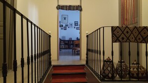 A staircase with black railings and a red carpet leading to a room with a bookshelf, a chair, and a patterned rug.