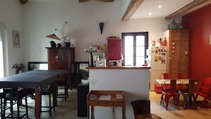 A cozy kitchen with wooden furniture, a dining table, and chairs. There is a refrigerator with magnets and a small island with a plant.