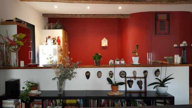 A room with a red wall, wooden ceiling beams, a white door, and a wooden counter with various items.