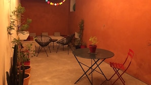 A cozy outdoor seating area with a round table and chairs, surrounded by potted plants and string lights.
