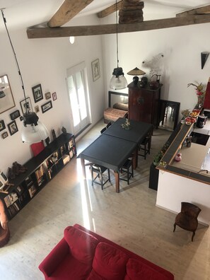 A spacious living room with a dining area, a red sofa, a wooden ceiling, and a bookshelf filled with books and decorative items.