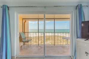 A room with a sliding glass door leading to a balcony with beach views.