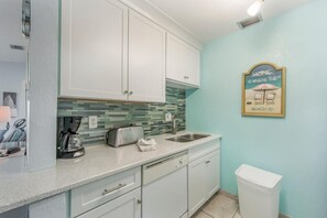 A kitchen with white cabinets, a tiled backsplash, a coffee maker, a toaster, and a sink.