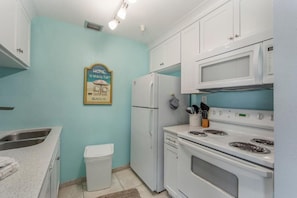 A compact kitchen with white appliances, a stainless steel sink, and a trash bin.