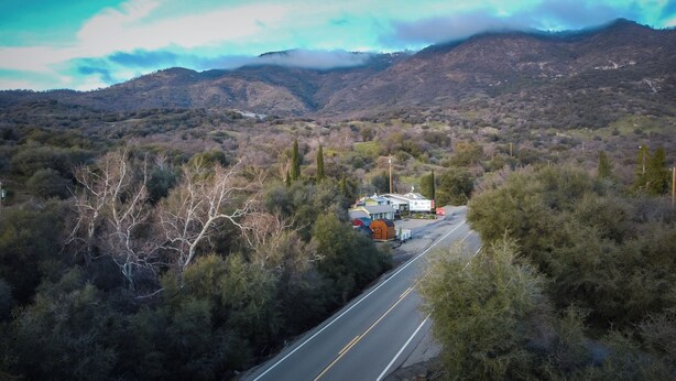 A remote road with a small building complex, surrounded by dense forest and mountains.