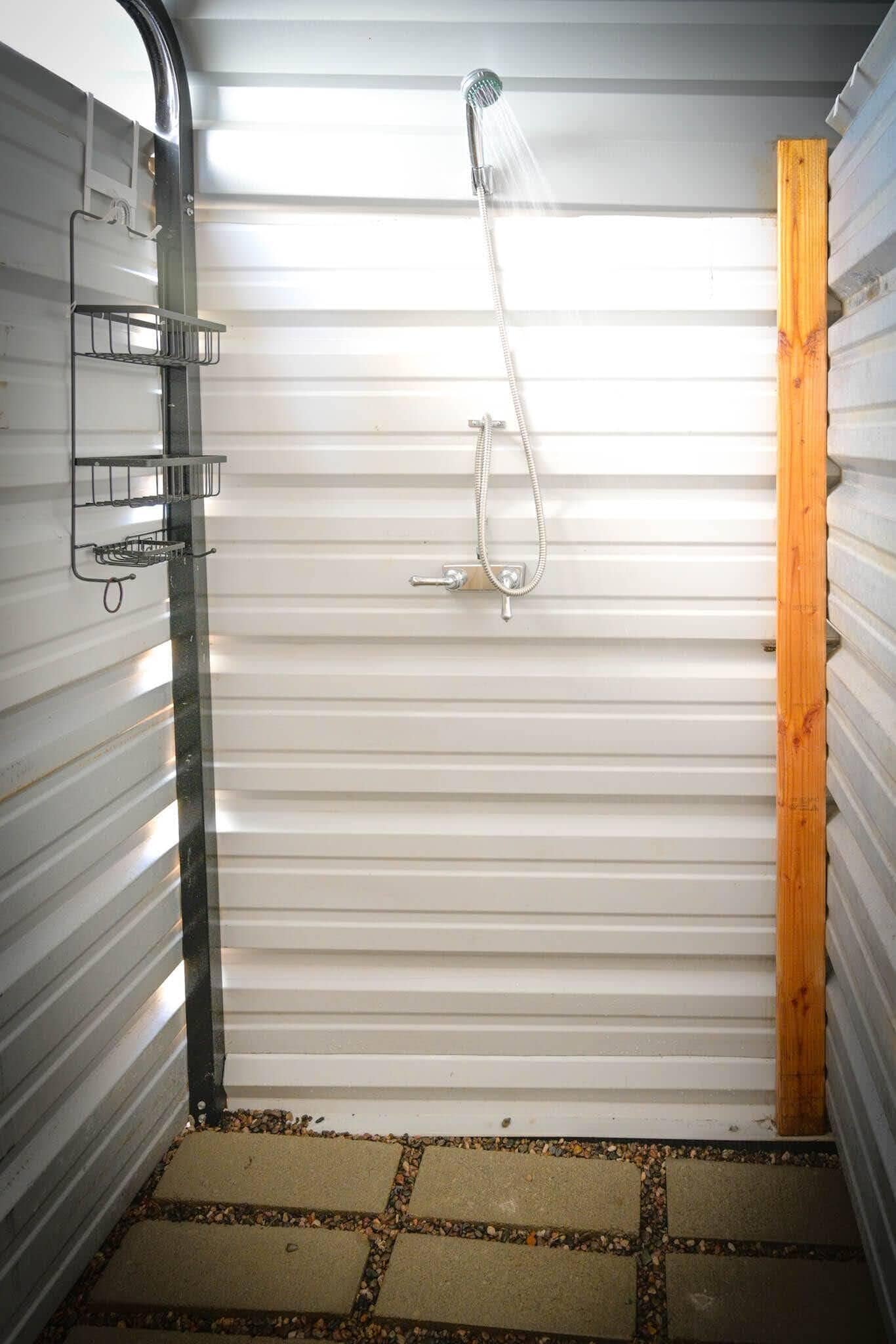 A small, enclosed shower area with a showerhead and a metal shelf.