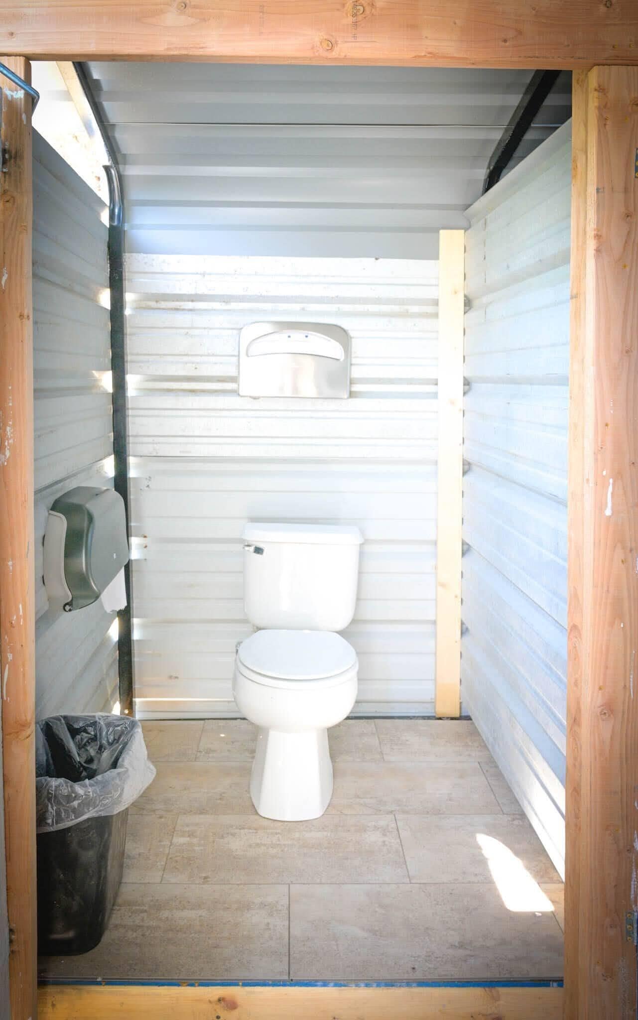 Une petite salle de bain fermée, équipée de toilettes, d’un sèche-mains et d’une poubelle.
