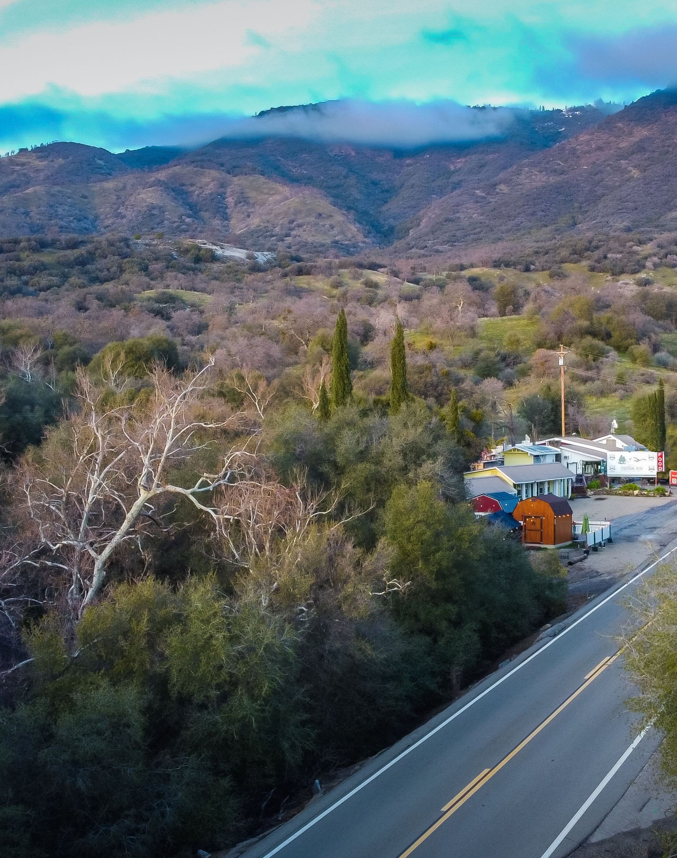 A road with a building labeled "Sierra Inn" on the right, surrounded by trees and hills.