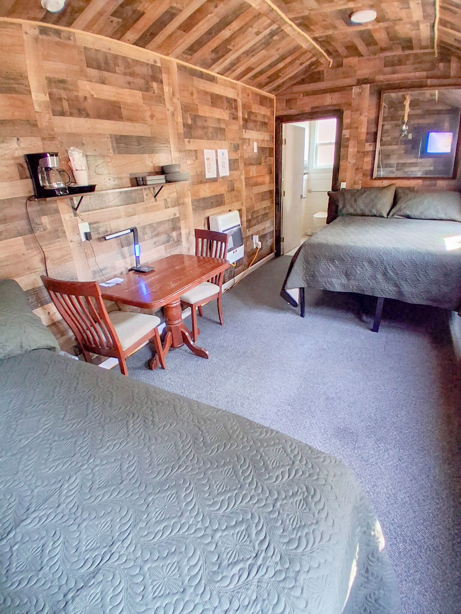 Une pièce confortable avec un plafond en bois, un lit, un bureau avec une chaise et une petite table avec une lampe.