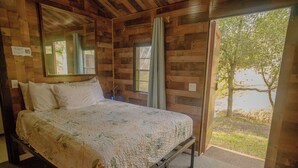 Ein Zimmer aus Holz mit einem Bett, einem Fenster und Blick auf einen Baum.